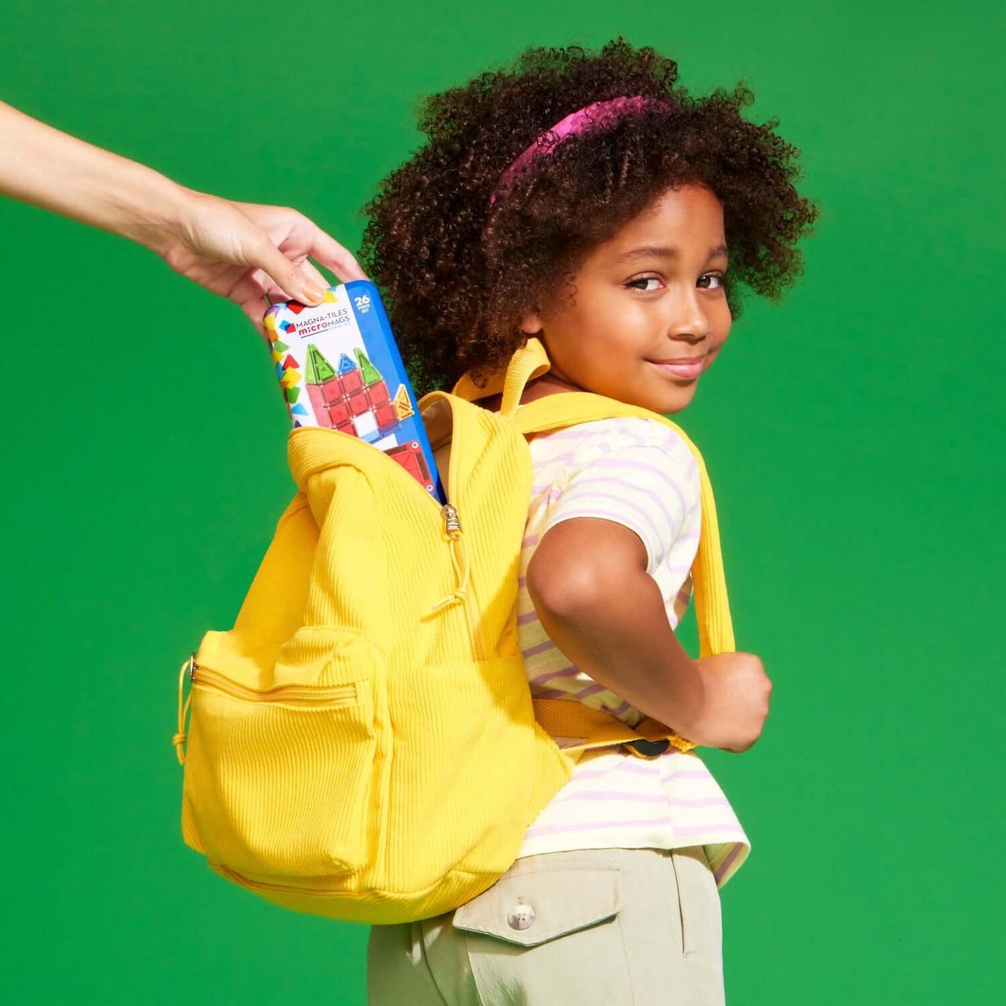 Child with a yellow backpack receiving a colorful book against a green background