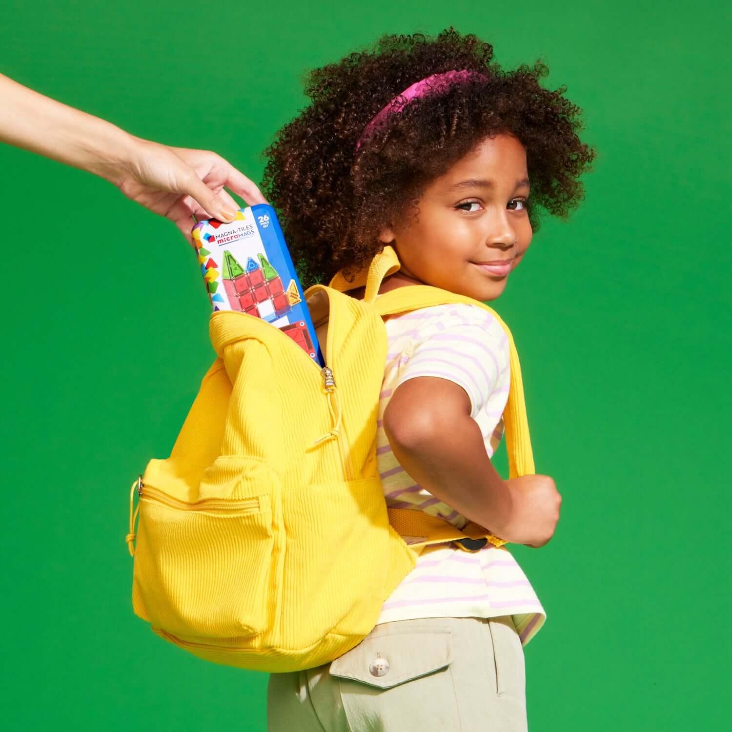 Child with a yellow backpack receiving a colorful book against a green background