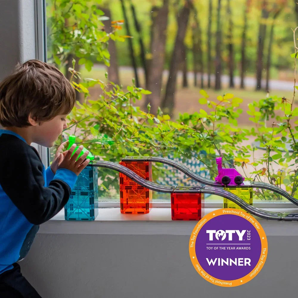 Child playing with a toy train set by a window with greenery outside