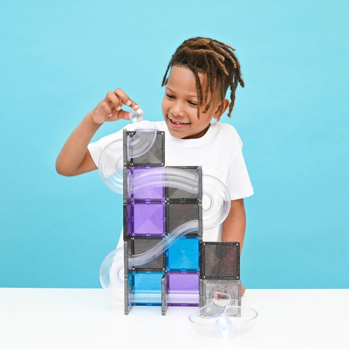 Young boy with dreadlocks smiling and building a clear magnetic marble run tower