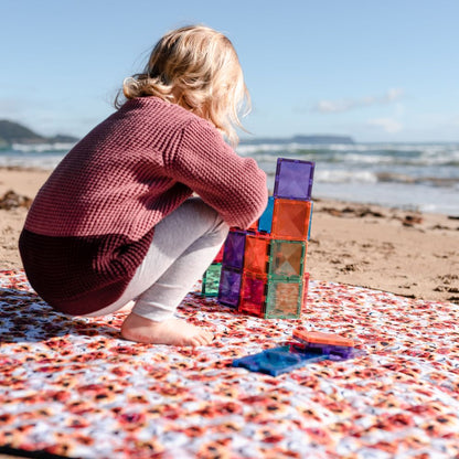 Child playing with colorful magnetic tiles on the beach, building creative structures with STEM learning toys.