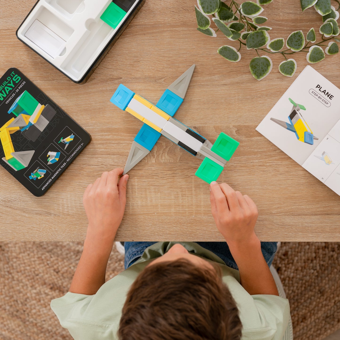 Child's hands are shown assembling a toy airplane made of colorful building blocks